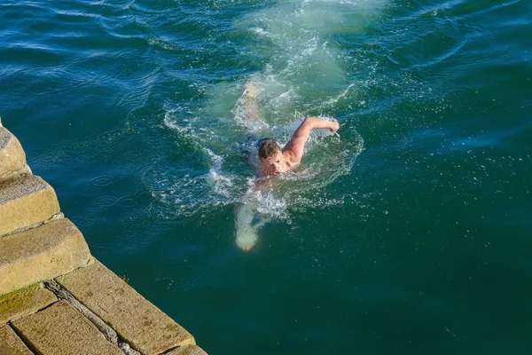 Joven nada en el mar cerca del muelle — Foto de Stock