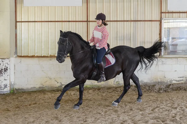 woman is riding a horse on a training ground