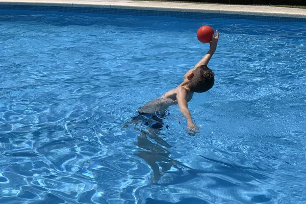 Мальчик в прыжке ловит мяч, играющий в бассейне — стоковое фото