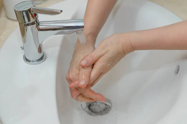 view of female hands in soapy foam under tap water close-up