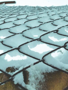 Iron net fence covered snow. Metal rusty fence-mesh netting in the snow. Close-up shot of snow on a fence. Lattice fence covered with fresh snow. White background texture. Winter background.