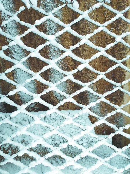 Iron net fence covered snow. Metal rusty fence-mesh netting in the snow. Close-up shot of snow on a fence. Lattice fence covered with fresh snow. White background texture. Winter background.