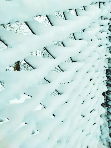 Iron net fence covered snow. Metal rusty fence-mesh netting in the snow. Close-up shot of snow on a fence. Lattice fence covered with fresh snow. White background texture. Winter background.