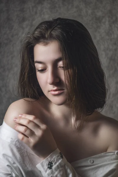 Portrait of a beautiful model in a white shirt. The delicate female part of the body is open. Bare neck and shoulders. Sexy girl