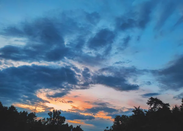 暖かい日没の太陽の光で照らされた絵のような雲 夕方の太陽の光で照らされた劇的な空の雲とカラフルな日没の空 日没時の田舎道 — ストック写真