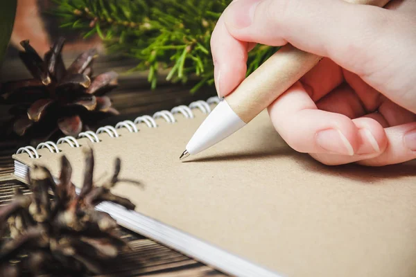 Weibliche Hand, Stift, Notizbuch, auf dem Hintergrund der Weihnachtsdekoration — Stockfoto