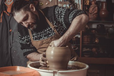 elderly man making pot using pottery wheel in studio clipart