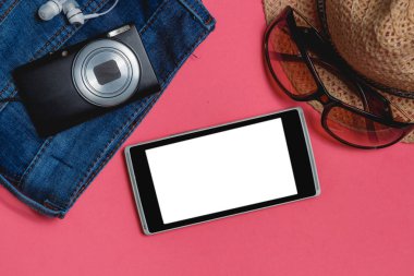 Smartphone, elbiseler, güneş gözlüğü, fotoğraf kamera, pembe bir arka plan üzerinde kahverengi şapka. En iyi görünümü seyahat kavramı alay kadar.