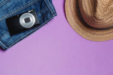 Giysi, fotoğraf makinesi, kahverengi şapka Lila zemin üzerine. Üstten Görünüm seyahat kavramı ile boşaltmak.