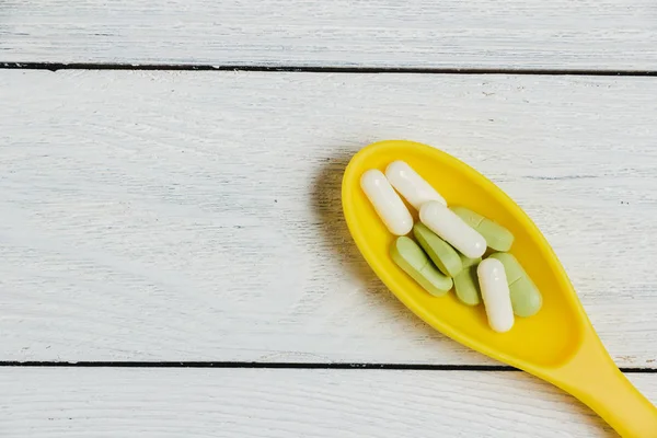 Sortiment Pillen, Tabletten und Kapseln in gelbem Löffel auf Holztisch. — Stockfoto