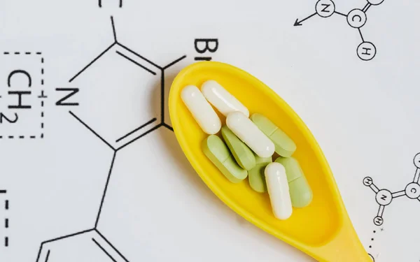 Sortiment an Pillen, Tabletten und Kapseln in gelbem Löffel auf weißem Hintergrund mit chemischer Formel. — Stockfoto