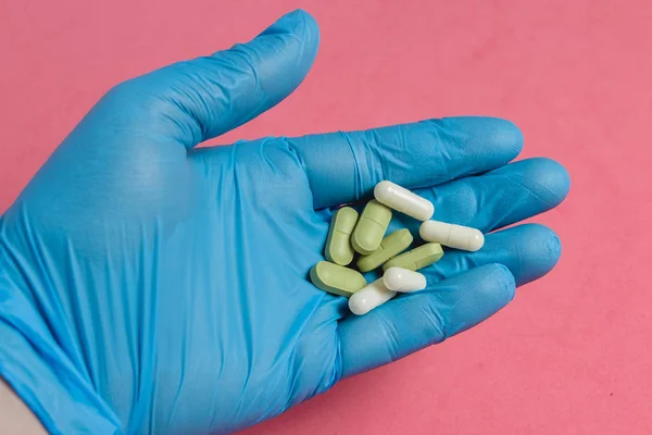 Sortiment an Pillen, Tabletten und Kapseln in blauem Handschuh vor rosa Hintergrund. — Stockfoto