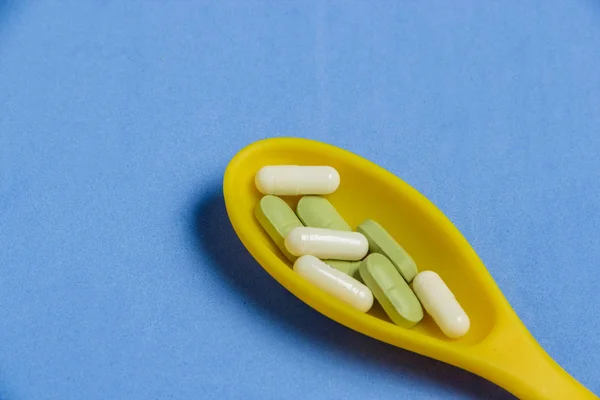 Pills and Capsules in Yellow Spoon on Blue Table. — Stock Photo, Image