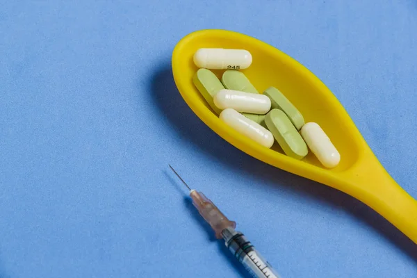 Асортимент таблеток і капсул в жовтий ложку, шприц на синьому фоні. — стокове фото