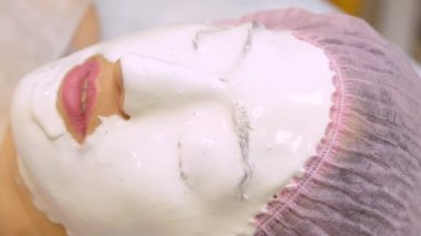 Güzellik salonundaki genç kadın aljinat maskesi yapıyor. Nemlendirici, yumuşatıcı, yenilenen maske uygulaması. Yüzdeki yenilenme işlemi Darsonval 'dan önce. Tıbbi güzellik ekipmanları.
