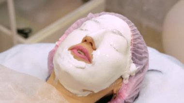 Güzellik salonundaki genç kadın aljinat maskesi yapıyor. Nemlendirici, yumuşatıcı, yenilenen maske uygulaması. Yüzdeki yenilenme işlemi Darsonval 'dan önce. Tıbbi güzellik ekipmanları.