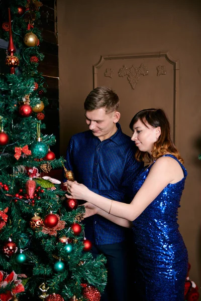 Young ordinary family of two. Young husband and wife near christmas tree. Happy young hetero couple decorate christmas tree at home. — Stock Photo, Image