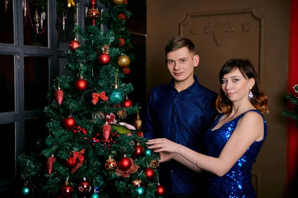 Young ordinary family of two. Young husband and wife near christmas tree. Happy young hetero couple decorate christmas tree at home. — Stock Photo, Image