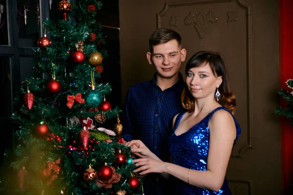 Молодая обычная семья из двух человек. Молодые муж и жена возле рождественской елки. Счастливая молодая гетеросексуальная пара украшает елку дома . — стоковое фото