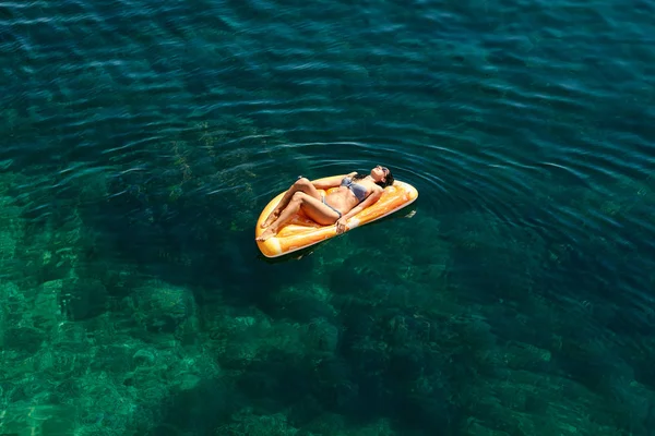 Тонка молода жінка в бікіні і сонцезахисних окулярах на повітряному матраці плаває у відкритому морі . — стокове фото