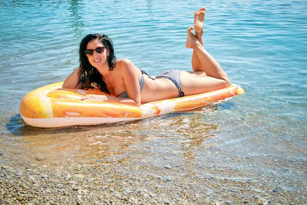 Slim young woman in bikini and sunglasses lies on the air mattress near sea side.