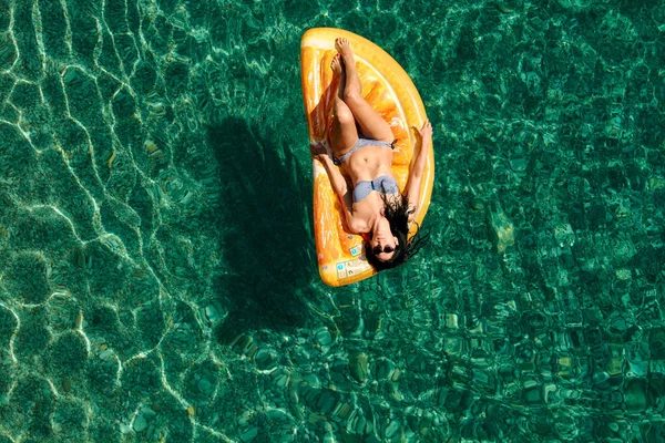 Bikinili sıska genç bir kadın ve şişme yatakta güneş gözlüğü açık denizde yüzüyor..