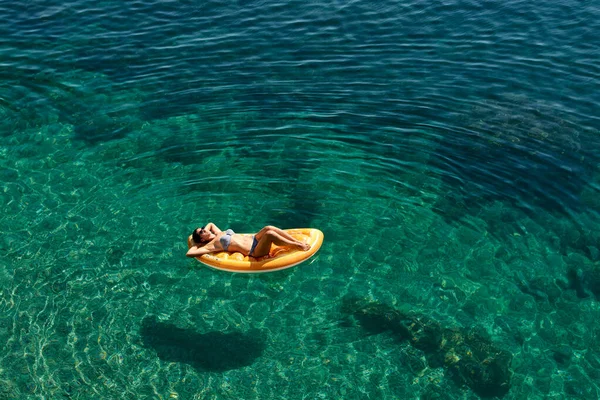 Bikinili sıska genç bir kadın ve şişme yatakta güneş gözlüğü açık denizde yüzüyor.. — Stok fotoğraf