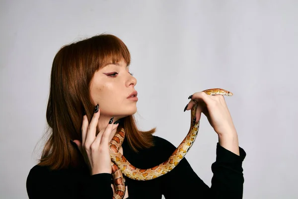 Beautiful woman in black bodywear and snake. Ginger model girl with fashion perfect make up. High end retouch. White background. Young woman with perfect fresh skin. Woman with snake around her.