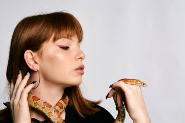 Siyah elbiseli ve yılanlı güzel bir kadın. Mükemmel makyajlı kızıl model kız. Üst düzey rötuş. Beyaz arka plan. Taze ciltli genç bir kadın. Etrafında yılan olan bir kadın..