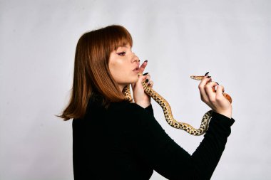 Siyah elbiseli ve yılanlı güzel bir kadın. Mükemmel makyajlı kızıl model kız. Üst düzey rötuş. Beyaz arka plan. Taze ciltli genç bir kadın. Etrafında yılan olan bir kadın..