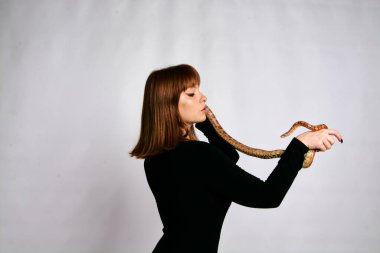 Siyah elbiseli ve yılanlı güzel bir kadın. Mükemmel makyajlı kızıl model kız. Üst düzey rötuş. Beyaz arka plan. Taze ciltli genç bir kadın. Etrafında yılan olan bir kadın..