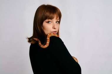 Siyah elbiseli ve yılanlı güzel bir kadın. Mükemmel makyajlı kızıl model kız. Üst düzey rötuş. Beyaz arka plan. Taze ciltli genç bir kadın. Etrafında yılan olan bir kadın..