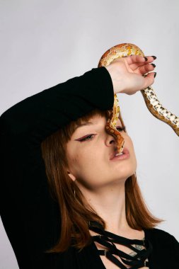 Siyah elbiseli ve yılanlı güzel bir kadın. Mükemmel makyajlı kızıl model kız. Üst düzey rötuş. Beyaz arka plan. Taze ciltli genç bir kadın. Etrafında yılan olan bir kadın..