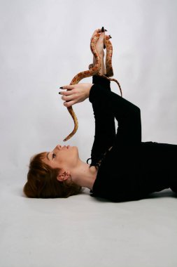 Siyah elbiseli ve yılanlı güzel bir kadın. Mükemmel makyajlı kızıl model kız. Üst düzey rötuş. Beyaz arka plan. Taze ciltli genç bir kadın. Etrafında yılan olan bir kadın..