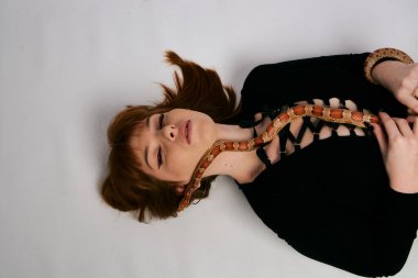 Siyah elbiseli ve yılanlı güzel bir kadın. Mükemmel makyajlı kızıl model kız. Üst düzey rötuş. Beyaz arka plan. Taze ciltli genç bir kadın. Etrafında yılan olan bir kadın..