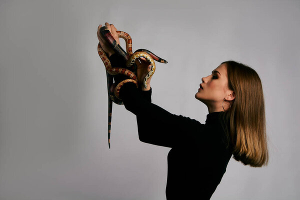 Красивая женщина в черной одежде и змее. Блондинка модель девушка с модным идеальным макияжем. High end retouch. Белый фон. Молодая женщина с совершенно свежей кожей. Женщина со змеей вокруг лица
.