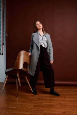 Genç bağımsız kadının mininalizm stili klasik stüdyo fotoğraf seti. Klasik takım elbiseli, siyah ayakkabılı ve gri ceketli güzel bir bayan. Klasik sandalye. Kadın kıyafetleri. Şık kıyafetler..