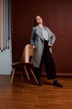 Genç bağımsız kadının mininalizm stili klasik stüdyo fotoğraf seti. Klasik takım elbiseli, siyah ayakkabılı ve gri ceketli güzel bir bayan. Klasik sandalye. Kadın kıyafetleri. Şık kıyafetler..