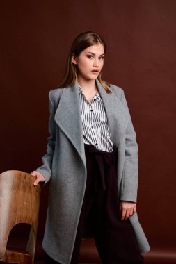 Genç bağımsız kadının mininalizm stili klasik stüdyo fotoğraf seti. Klasik takım elbiseli, siyah ayakkabılı ve gri ceketli güzel bir bayan. Klasik sandalye. Kadın kıyafetleri. Şık kıyafetler..