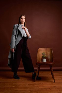 Genç bağımsız kadının mininalizm stili klasik stüdyo fotoğraf seti. Klasik takım elbiseli, siyah ayakkabılı ve gri ceketli güzel bir bayan. Klasik sandalye. Kadın kıyafetleri. Şık kıyafetler..