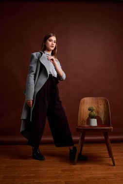 Genç bağımsız kadının mininalizm stili klasik stüdyo fotoğraf seti. Klasik takım elbiseli, siyah ayakkabılı ve gri ceketli güzel bir bayan. Klasik sandalye. Kadın kıyafetleri. Şık kıyafetler..