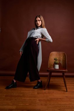 Genç bağımsız kadının mininalizm stili klasik stüdyo fotoğraf seti. Klasik takım elbiseli, siyah ayakkabılı ve gri ceketli güzel bir bayan. Klasik sandalye. Kadın kıyafetleri. Şık kıyafetler..