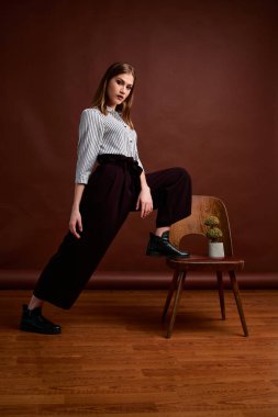 Genç bağımsız kadının mininalizm stili klasik stüdyo fotoğraf seti. Klasik takım elbiseli, siyah ayakkabılı ve gri ceketli güzel bir bayan. Klasik sandalye. Kadın kıyafetleri. Şık kıyafetler..