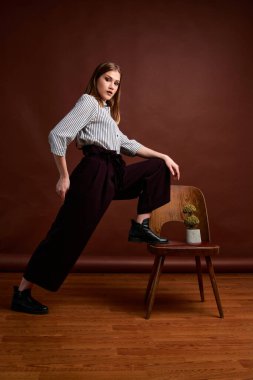 Genç bağımsız kadının mininalizm stili klasik stüdyo fotoğraf seti. Klasik takım elbiseli, siyah ayakkabılı ve gri ceketli güzel bir bayan. Klasik sandalye. Kadın kıyafetleri. Şık kıyafetler..