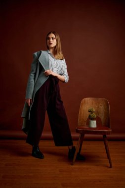 Genç bağımsız kadının mininalizm stili klasik stüdyo fotoğraf seti. Klasik takım elbiseli, siyah ayakkabılı ve gri ceketli güzel bir bayan. Klasik sandalye. Kadın kıyafetleri. Şık kıyafetler..