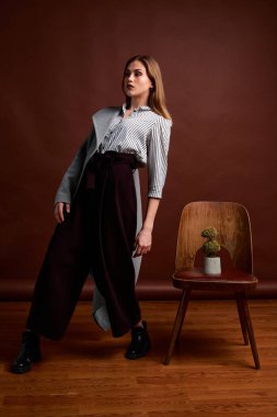 Genç bağımsız kadının mininalizm stili klasik stüdyo fotoğraf seti. Klasik takım elbiseli, siyah ayakkabılı ve gri ceketli güzel bir bayan. Klasik sandalye. Kadın kıyafetleri. Şık kıyafetler..