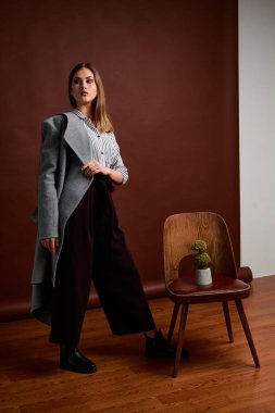 Genç bağımsız kadının minimalizm stili klasik stüdyo fotoğraf seti. Klasik takım elbiseli, siyah ayakkabılı ve gri ceketli güzel bir bayan. Klasik sandalye. Kadın kıyafetleri. Şık kıyafetler..