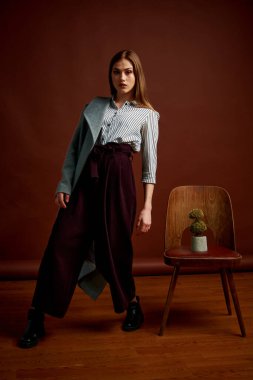 Genç bağımsız kadının minimalizm stili klasik stüdyo fotoğraf seti. Klasik takım elbiseli, siyah ayakkabılı ve gri ceketli güzel bir bayan. Klasik sandalye. Kadın kıyafetleri. Şık kıyafetler..