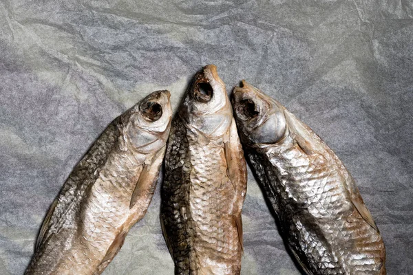 Tre torkade fiskar på gammalt skrynkligt papper. Öl mellanmål. Högsta tittarsiffror — Stockfoto