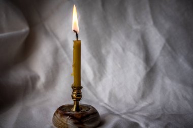 Buruşuk keten kumaşın arka planında yanan bir mum olan şamdan. Koyu renk.